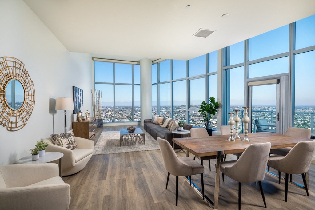 a living and dining area with a wooden table and chairs and large windows with a city view