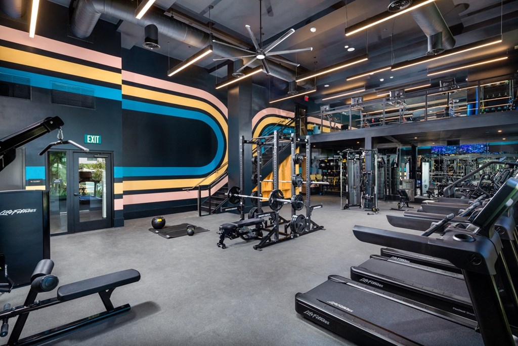 a gym with cardio machines and weights on the floor and a wall painted with stripes