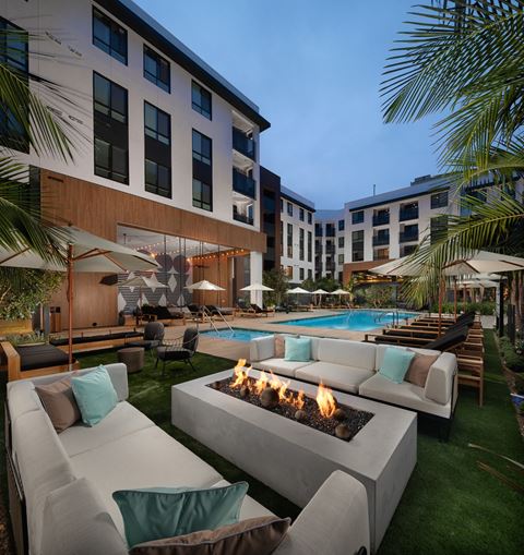 an outdoor lounge area with couches and chairs and a fire pit with a pool in the