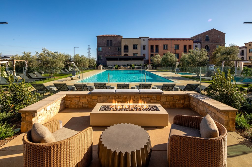 an outdoor patio with a firepit and chairs with a pool in the background