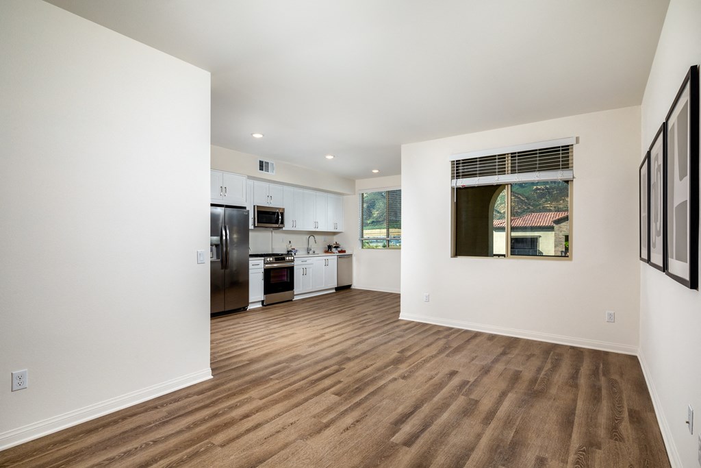 a living room and kitchen with white walls and wood floors