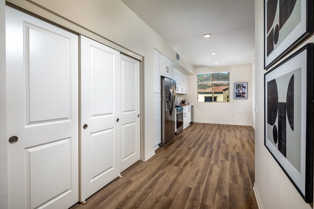 a hallway with white doors and a kitchen with a refrigerator and a sink
