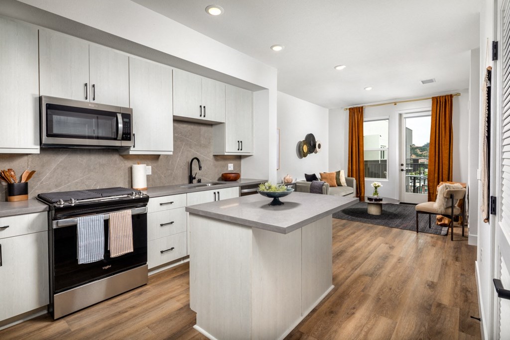a kitchen and living room with white cabinets and a large island with a granite countertop a kitchen and living room with white cabinets and a large island with a granite countertop at VORA LUX, San Diego, 92120