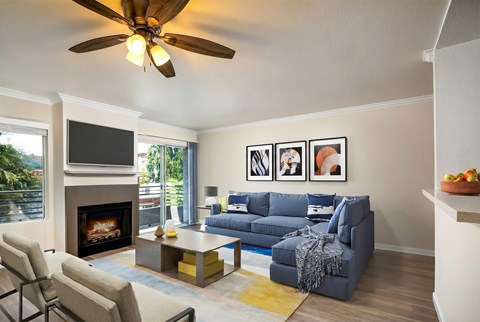 A living room with a fireplace, a grey couch, and a ceiling fan.
