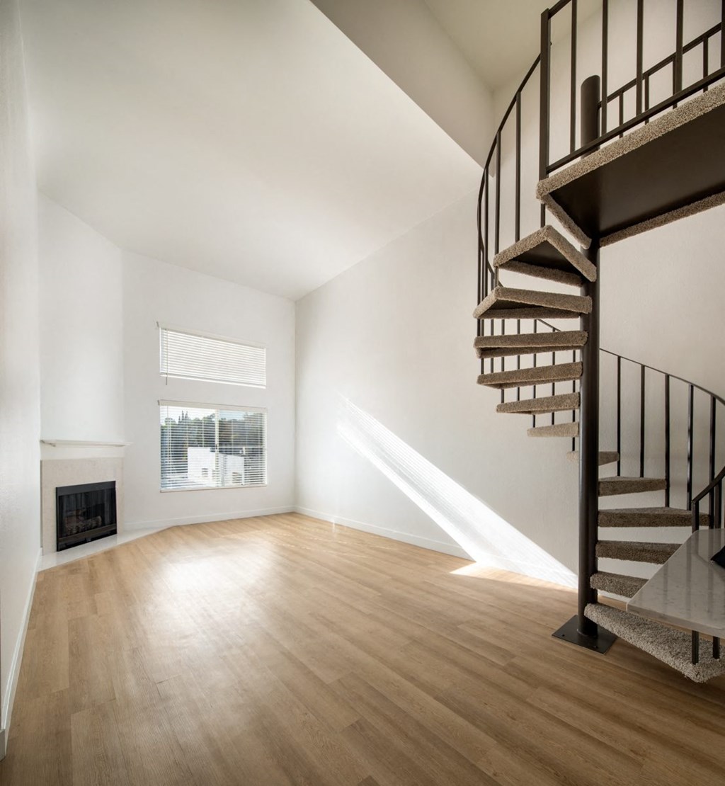 A wooden staircase with a metal railing leads up to a window in a white room.