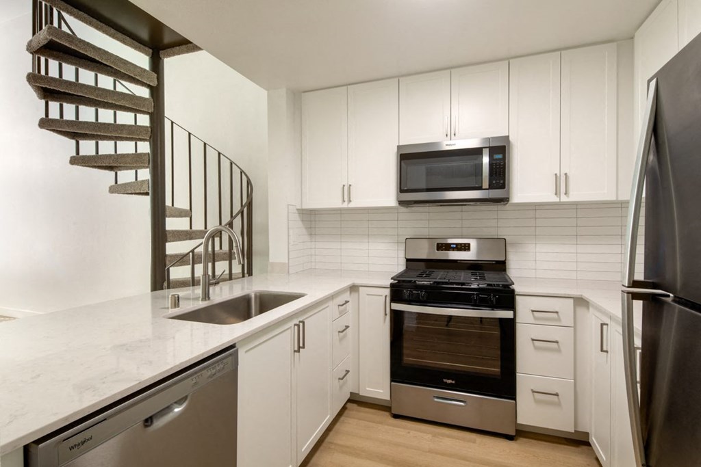 A modern kitchen with a stainless steel refrigerator, a microwave above the stove, and a spiral staircase.