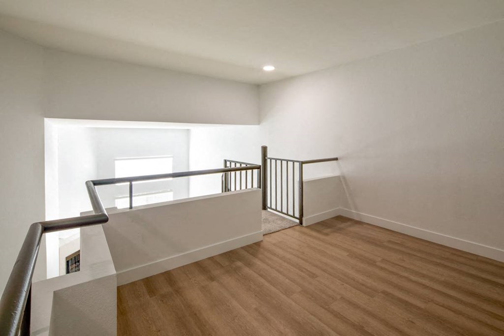 A room with wooden floors and a balcony with a metal railing.