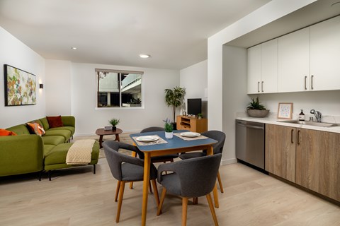 A modern dining room with a green couch, wooden chairs, and a table set for two.