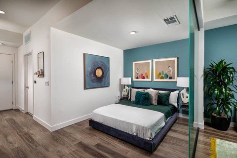 A bedroom with a bed, a painting, and a potted plant.