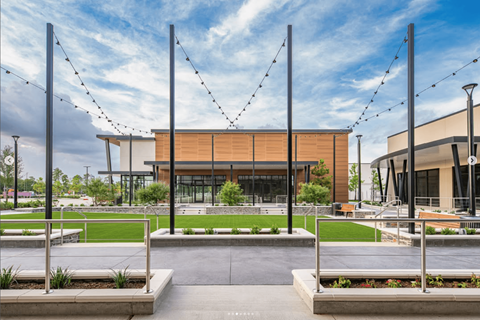 A modern building with a glass facade is surrounded by a grassy area and decorative string lights.