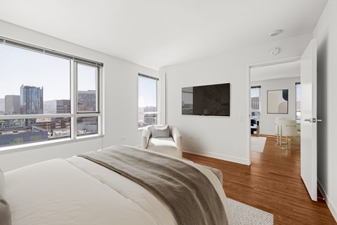 A bedroom with a large bed and a city view through the window.