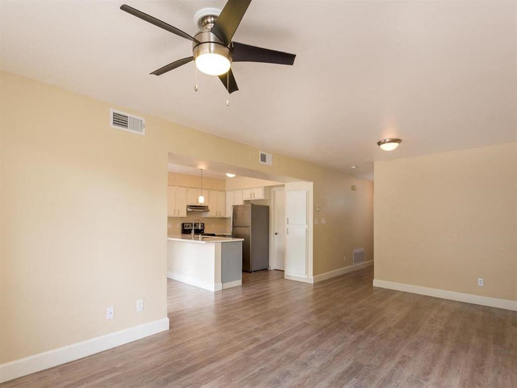 an empty living room with a ceiling fan and a kitchen