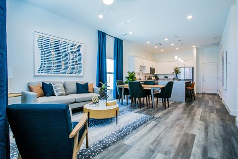 A modern living room with a grey sofa, a wooden coffee table, and a dining table with chairs.