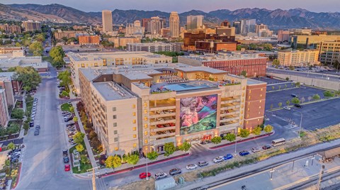 A large building with a mural on the side is surrounded by a parking lot and other buildings.