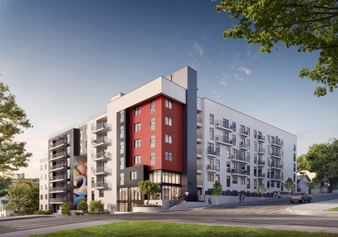 A modern apartment building with a red and white facade is surrounded by trees and a clear blue sky.