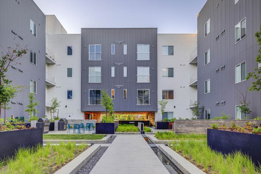 a walkway with benches and tables in front of an apartment building