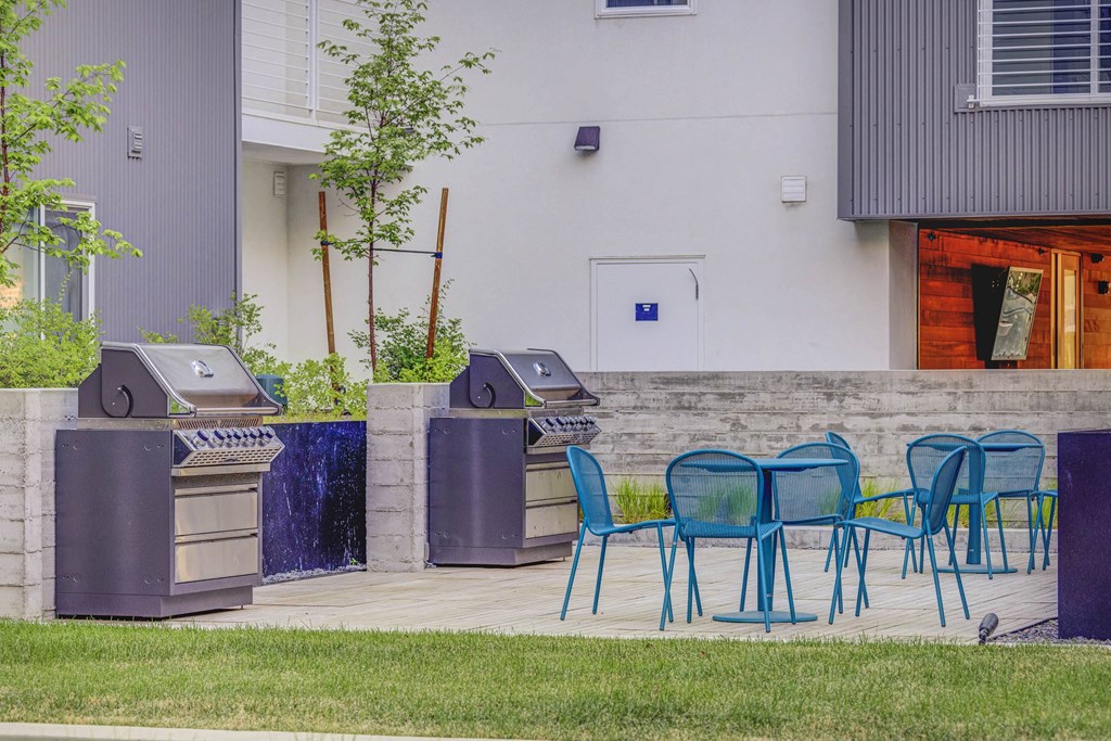 two bbq grills and blue chairs on a patio in front of a building