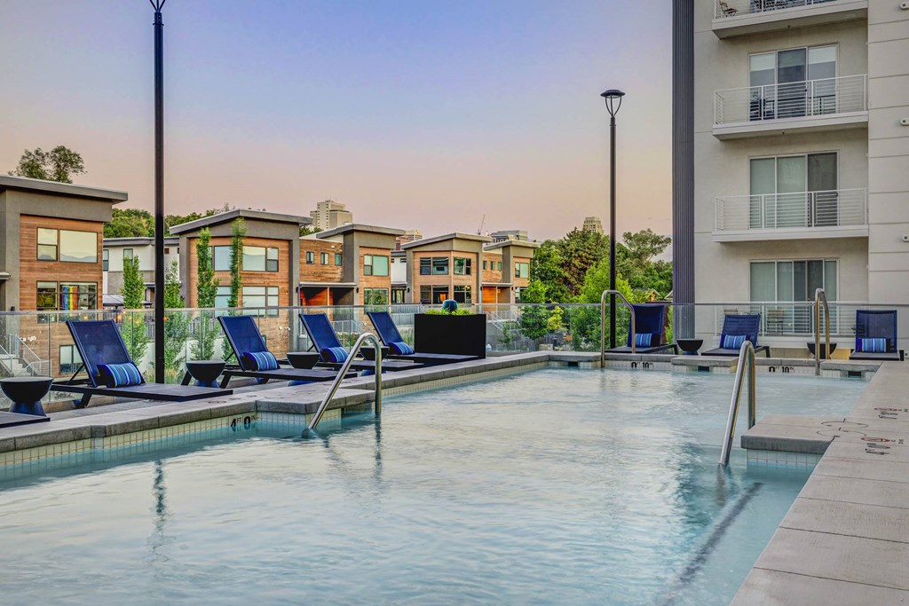 a swimming pool with blue lounge chairs and buildings in the background