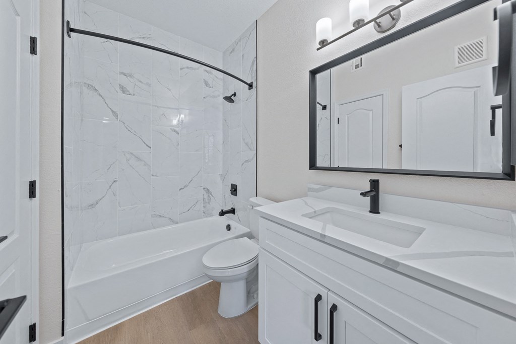 a bathroom with white cabinets and a white toilet next to a white bathtub with a shower