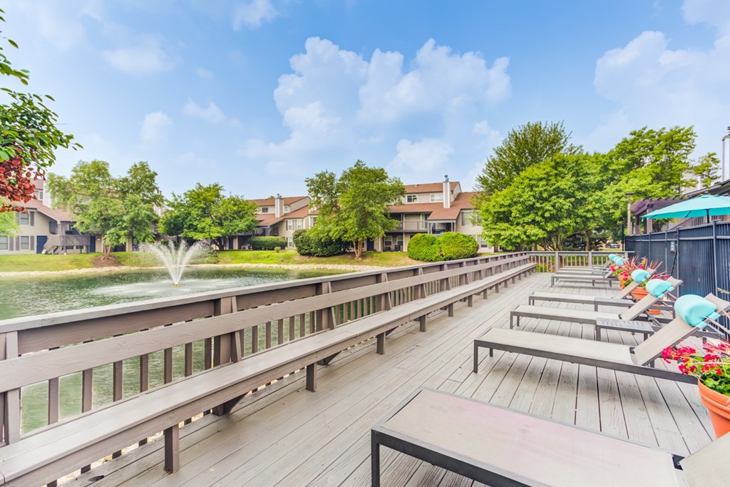 A wooden deck with benches overlooks a green lawn and trees.