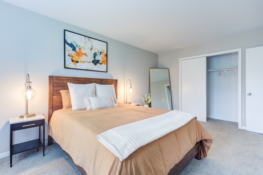 A bedroom with a bed, nightstand, and a painting on the wall.