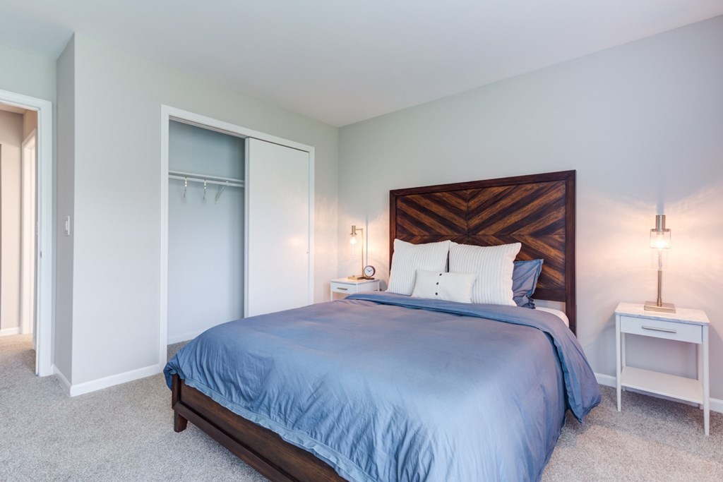 A bedroom with a blue bedspread and a wooden headboard.