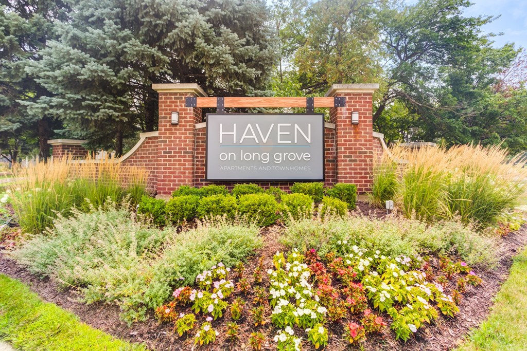 A sign that says Haven on a long grove in front of a brick wall.