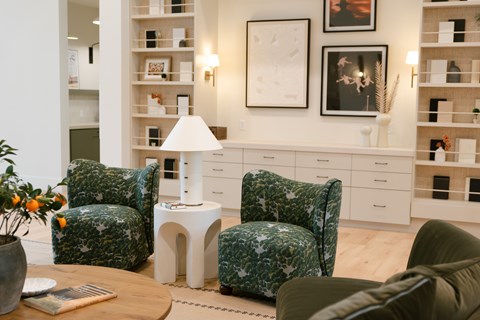 A living room with a green patterned chair and a white table with a lamp on it.