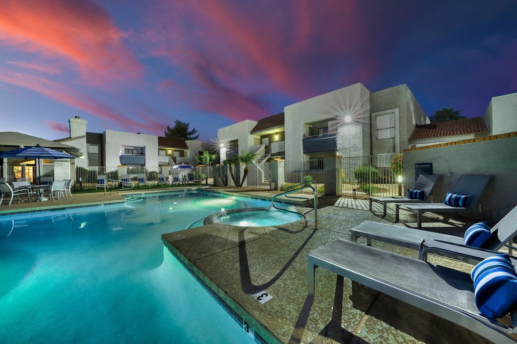 a large swimming pool with lounge chairs and umbrellas in front of a building