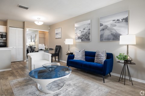 A living room with a blue couch and a glass coffee table.