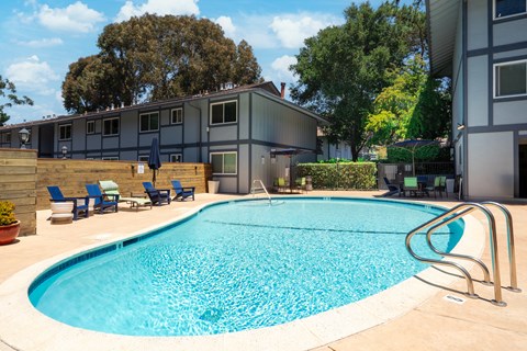 A swimming pool surrounded by chairs and trees.