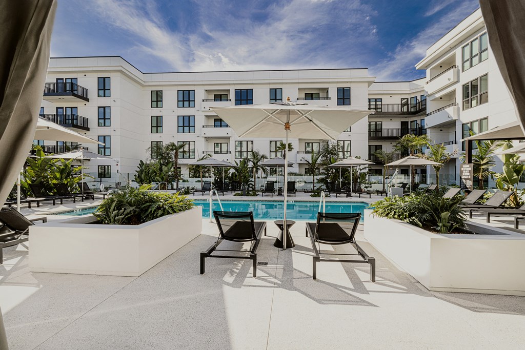 a pool with chairs and a table in front of an apartment building