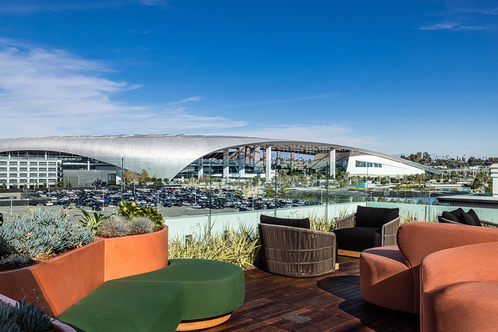 a roof top patio with chairs and plants and a view of a stadium