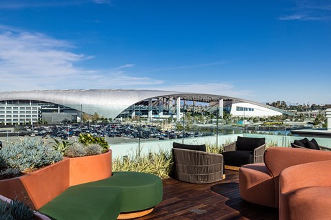 a roof top patio with chairs and plants and a view of a stadium