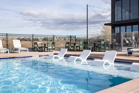 A pool with white chairs and a building in the background.