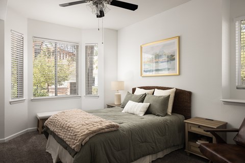 A bedroom with a bed, a ceiling fan, and a window with blinds.
