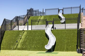 A playground with a white slide and black fencing.