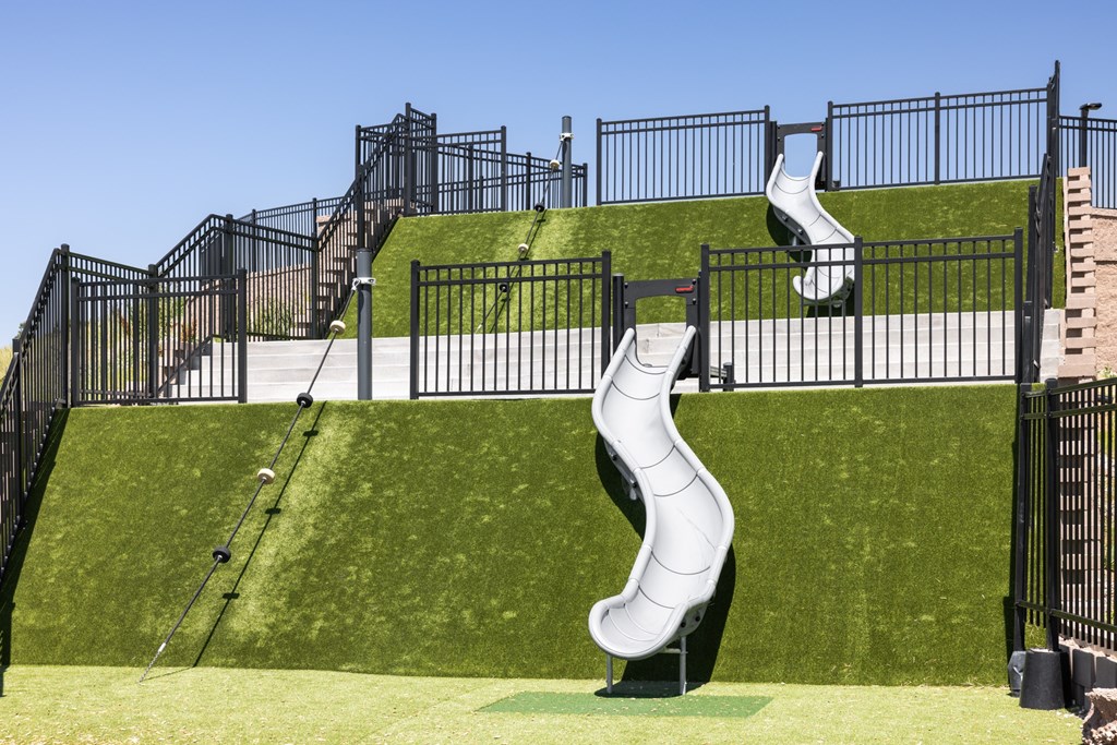 A playground with a white slide and black fencing.