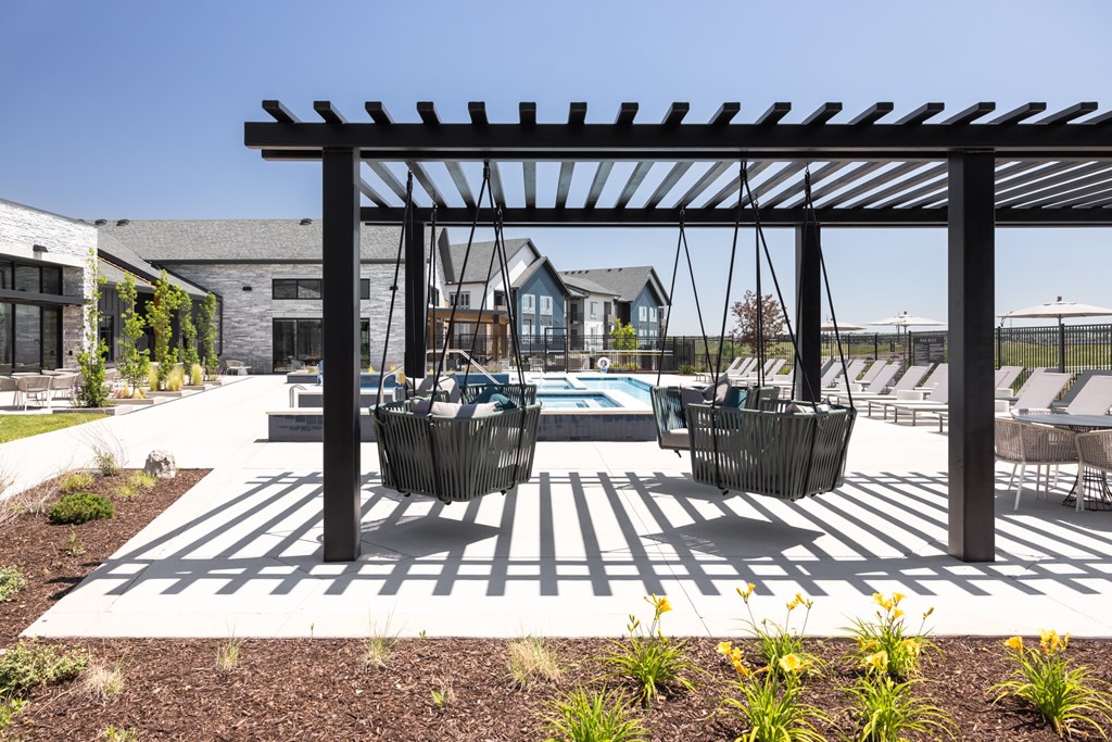 A patio with a pergola and chairs is surrounded by a garden.