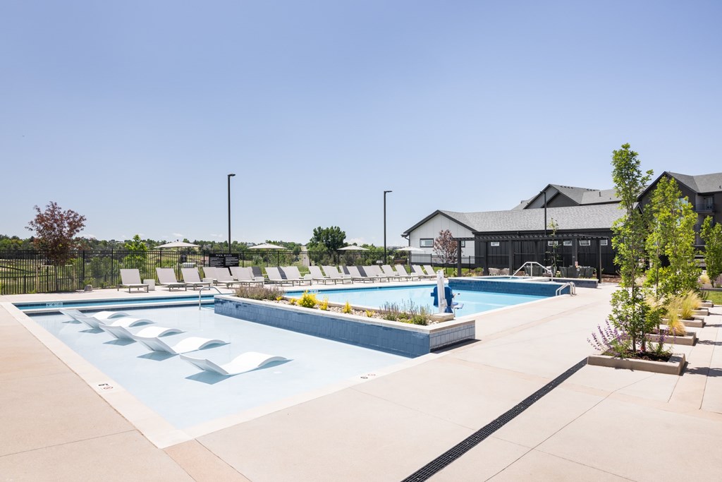 A large outdoor swimming pool with lounge chairs and a building in the background.