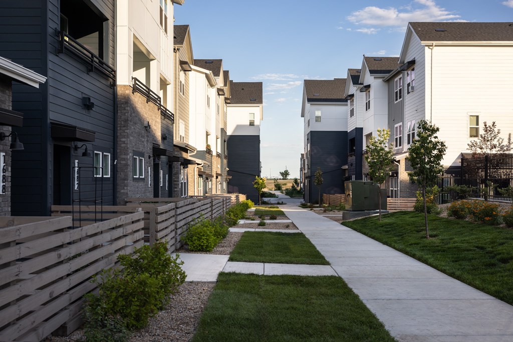 A row of modern townhouses with a sidewalk and landscaping in the foreground.