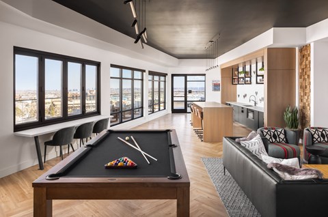 A billiard table is in the middle of a living room with a view of the city.