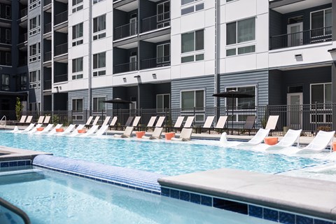 A swimming pool with lounge chairs in front of apartment buildings.