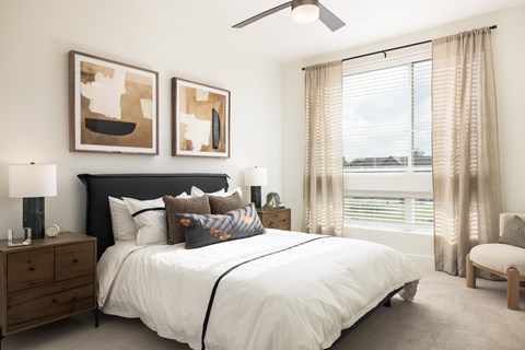 A bedroom with a large bed, a ceiling fan, and two abstract paintings on the wall.