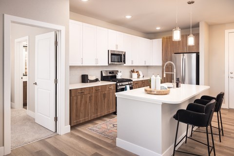 A kitchen with white cabinets and a white island with black chairs.