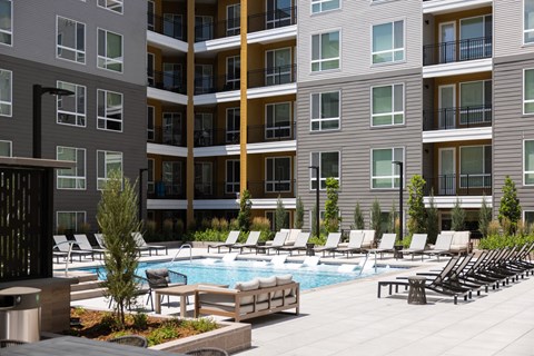 a pool with lounge chairs in front of an apartment building