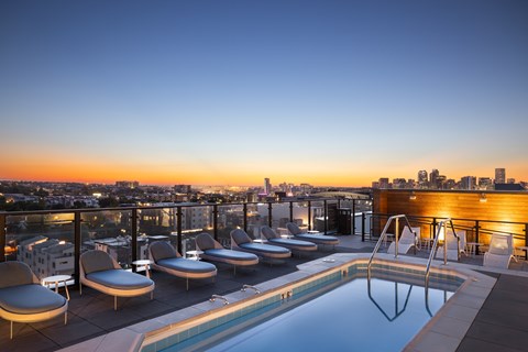 A rooftop pool with lounge chairs overlooking a city skyline at dusk.