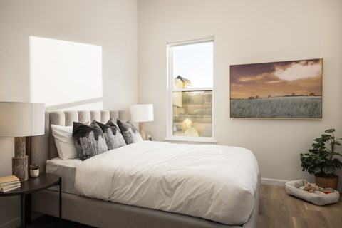 A bedroom with a large bed, a lamp, a potted plant, and a painting on the wall.