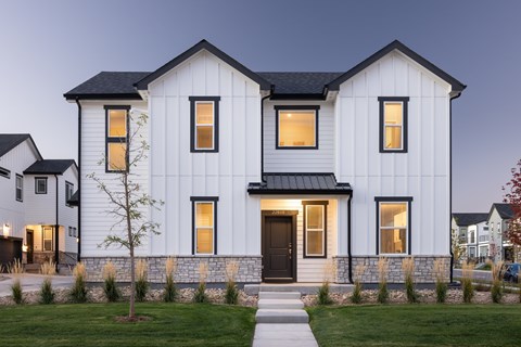 A white house with a black roof and a tree in front.