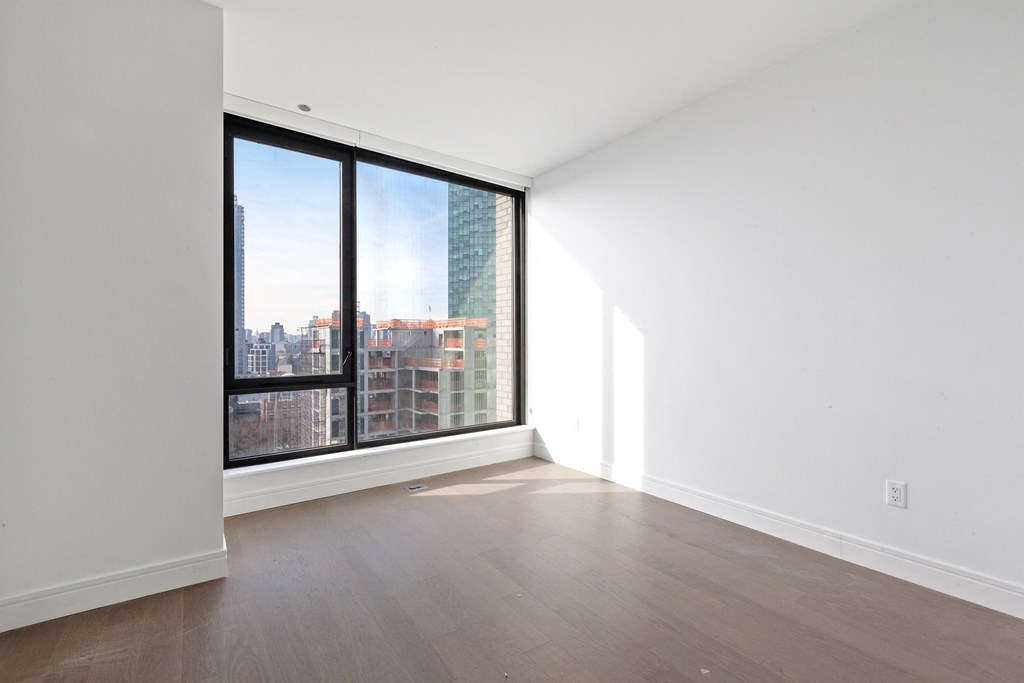 an empty living room with a large window and hardwood floors